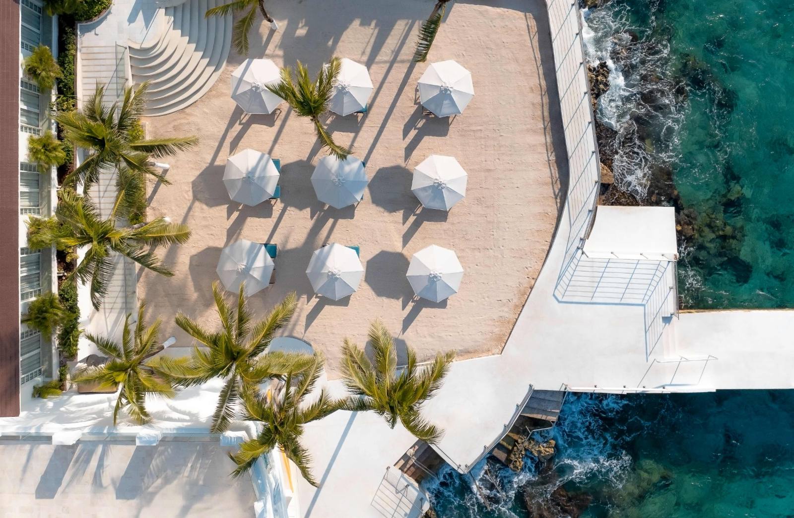 Straight down on the sun terrace: nine umbrellas, and reef water past the rail