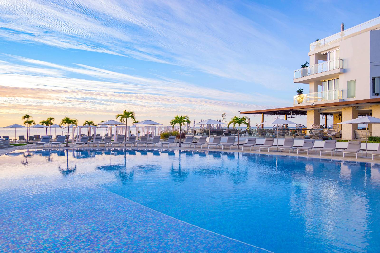 The main pool at sunrise: loungers all the way round, ocean past the palms
