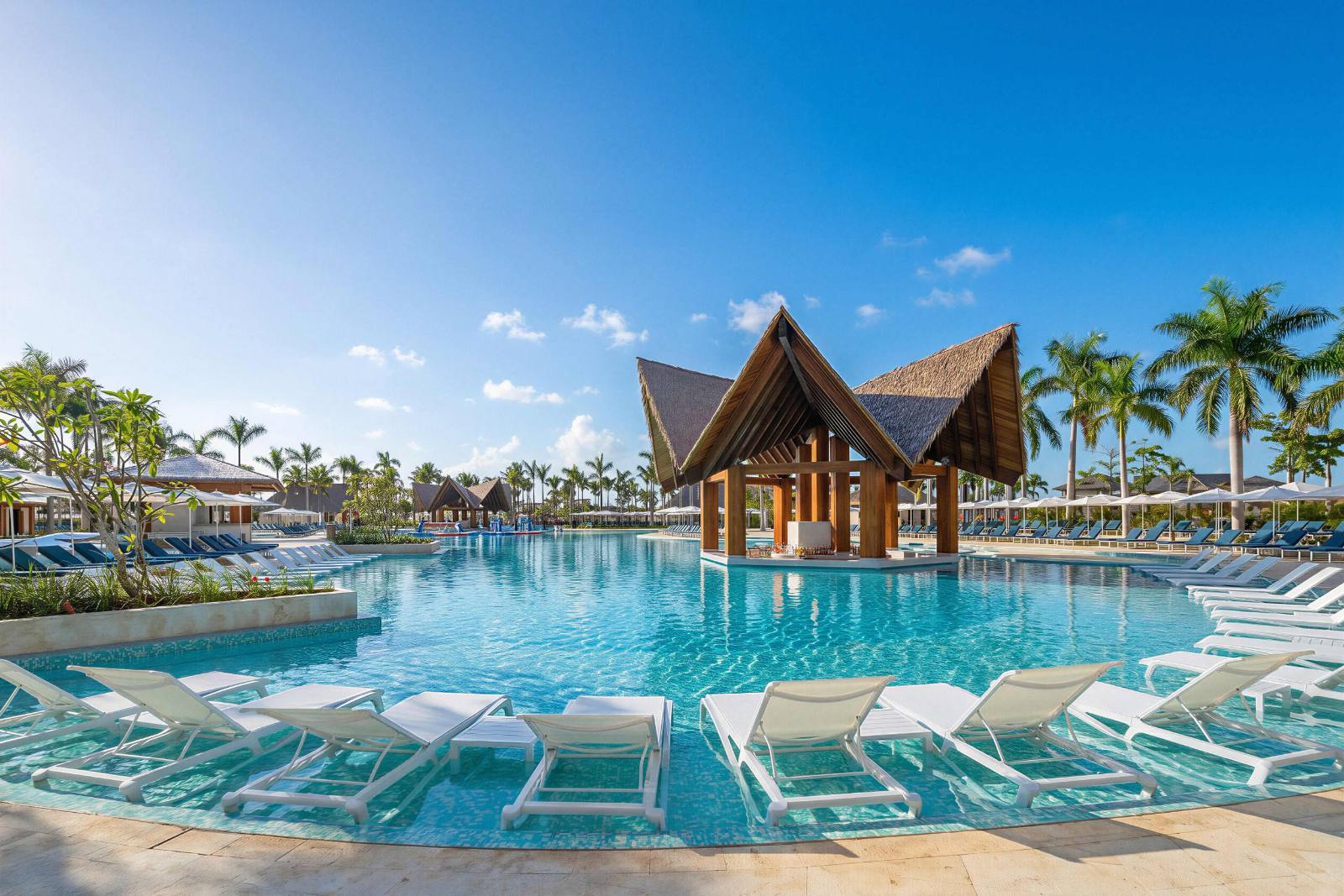 The main pool: in-water loungers on the near edge, thatched swim-up bar mid-pool