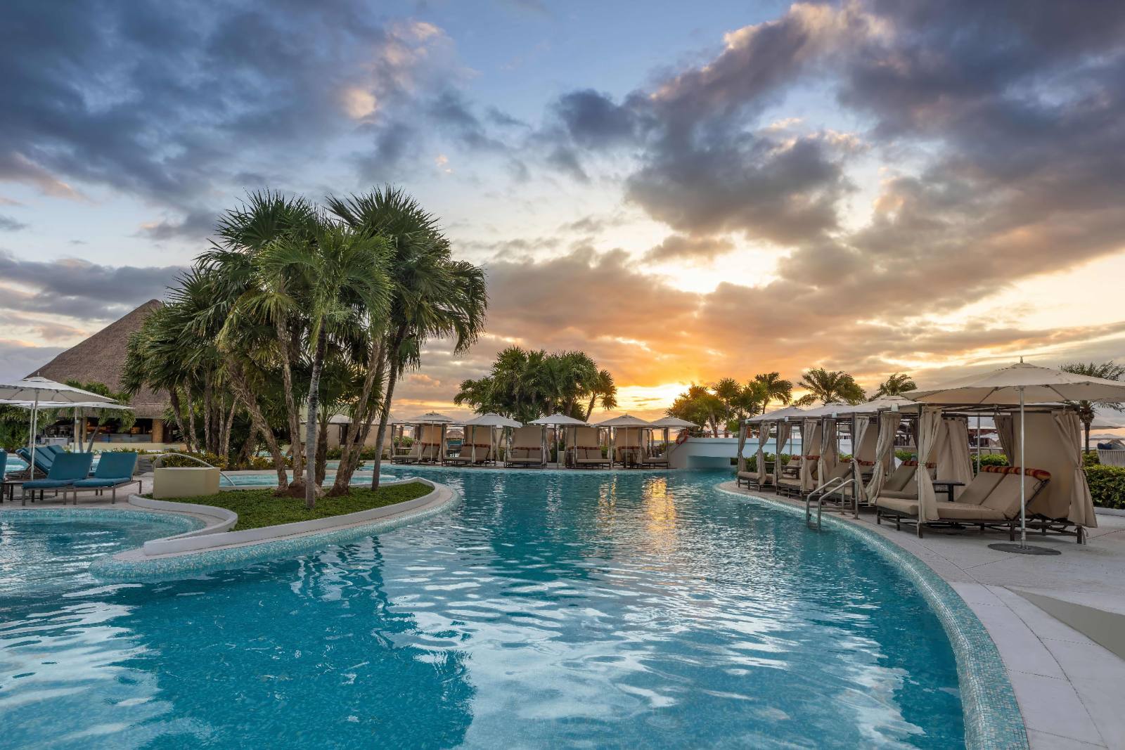 The pool deck at sunset: cabanas along one edge, five linked pools behind